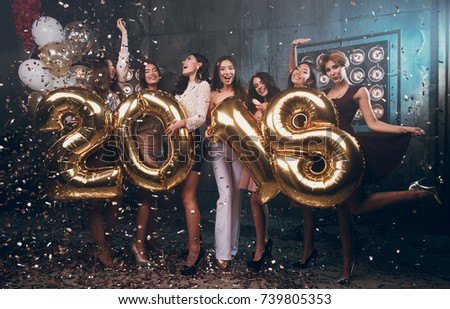 Celebrating New Year party. Group of cheerful young girls in beautiful wearing carrying gold colored numbers 2018 and throwing confetti