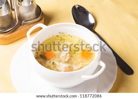 A chicken broth in white ware on the yellow tablecloth