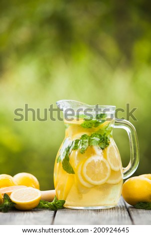 Preparation of the lemonade drink. Lemonade in the jug and lemons with mint on the table outdoor