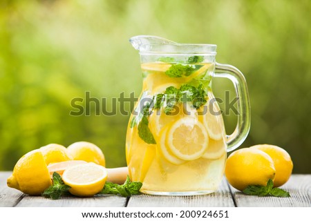 Preparation of the lemonade drink. Lemonade in the jug and lemons with mint on the table outdoor