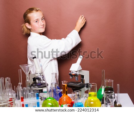 Schoolgirl with chalk standing near blackboard in the laboratory classes in chemistry and wants to white. Focus on the microscope