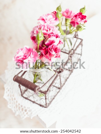 Pink flowers in glass bottles in metal basket. Vintage decor concept