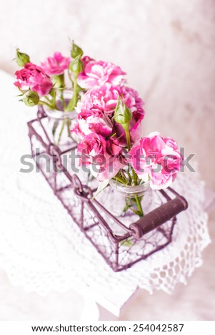 Pink flowers in glass bottles in metal basket. Vintage decor concept