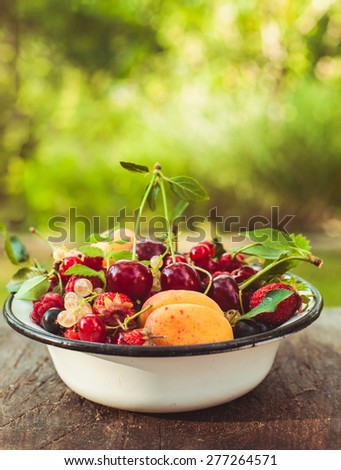 Summer fruits in enamelled metal bowl on wooden table