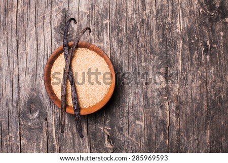 Vanilla sugar in a wooden bowl on a rustic background. Two vanilla pods on brown sugar