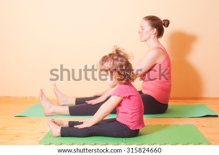 Mom and daughter doing yoga exercises on green rug