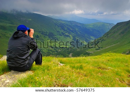 Beautiful mountains landscape with lake and clouds in Carpathian mountains and man with binoculars
