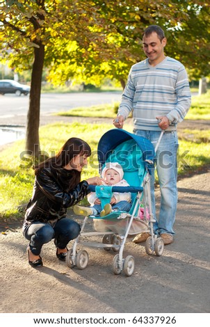 Happy family outdoor - mother, father and dauther are smiling in baby carriage