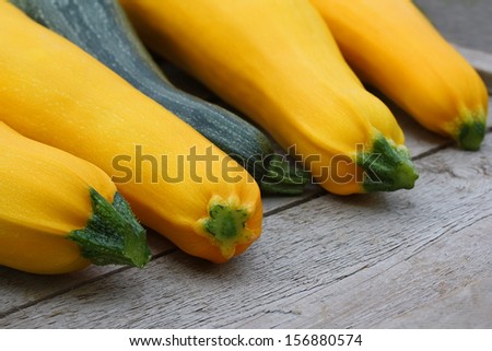 Four brightly yellow zucchini vegetable marrows and one green striped zucchini vegetable marrow on an old wooden background