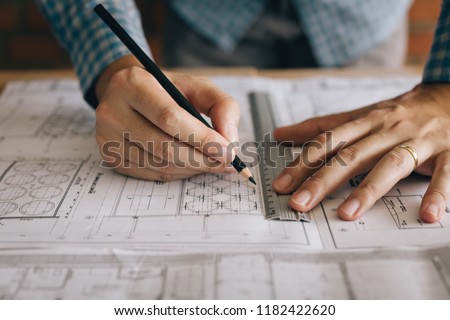 Interior designer or architect reviewing blueprints and holding pencil on desk at home office.