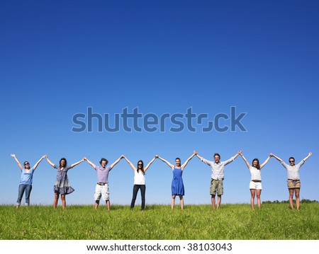 Group of friends holding hands in meadow under blue sky
