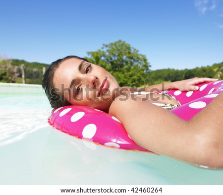Woman floating in a pink polka dot inner tube and smiling gently at the camera. Horizontal.