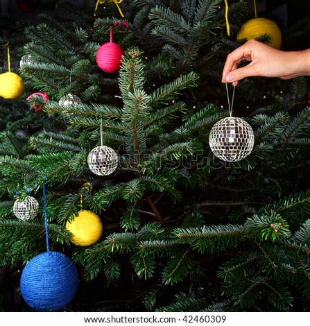 A hand is shown putting a disco ball ornament on a Christmas tree. Square format.