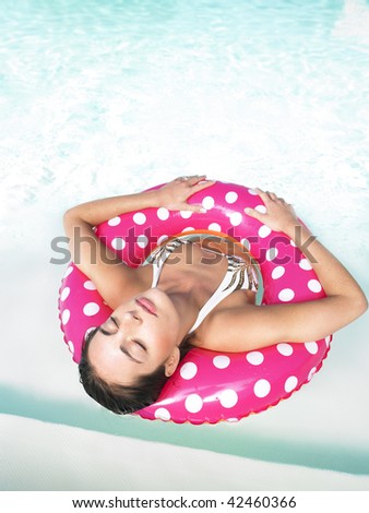 Woman floating in a pink polka dot inner tube with eyes closed. Vertical.