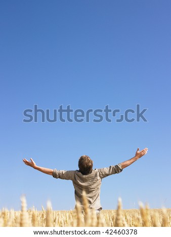 Man standing in wheat field with arms outstretched. Vertically framed shot.