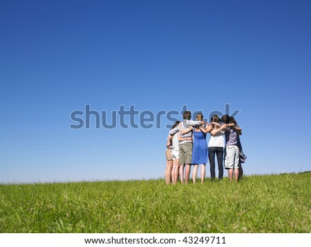 A group of people huddle in a field. Horizontally framed shot.
