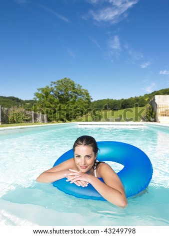 Woman floating in inner tube in pool and smiling at the camera. Vertical
