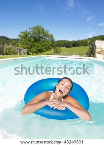 Woman floating in inner tube in pool and laughing. Vertical