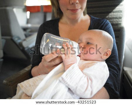 Mother feeds baby a bottle while traveling on train. Horizontally framed shot.
