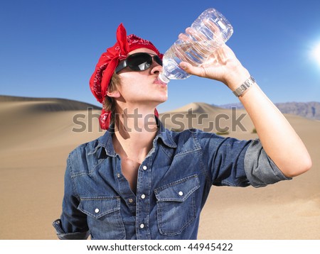 Young man in sunglasses wearing red bandana drinking a bottle of water. Horizontal shot.