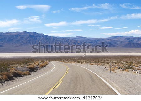 Two lane highway passing through desert flatland with mountains in background. Horizontal shot.