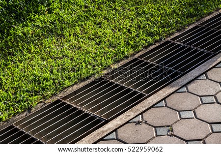 waterway and road - grass. Aqueduct between nature and city. iron grate of water drain in grass garden field. Steel rusty grating in the Grass garden and concrete. Manhole cover metal and way - grass.