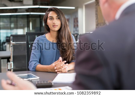 Focused Indian female customer meeting with financial advisor. Young beautiful candidate at job interview in modern office space. Business consulting or employment concept
