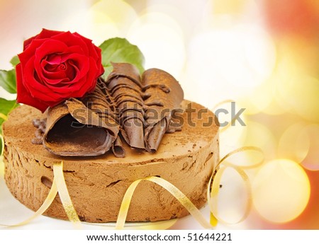 Birthday card with toffee cake and red rose over defocused lights.