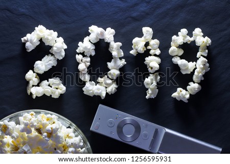 Popcorn closeup in the form of the number 2019 and the remote control from the TV on a dark background. Christmas and New Year holidays at home by the TV