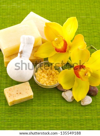 Massage ball with salt in bowl and orchid flowers, soap on green mat