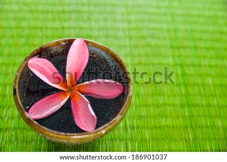Pink frangipani flower in bowl on green straw mat