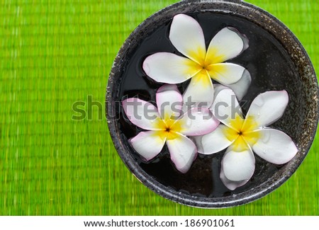 Three white frangipani flower in bowl on straw mat