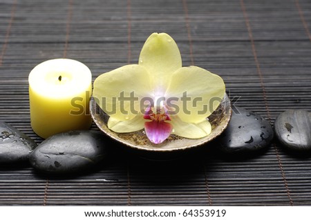 Yellow orchid flower in bowl and candle on zen pebble