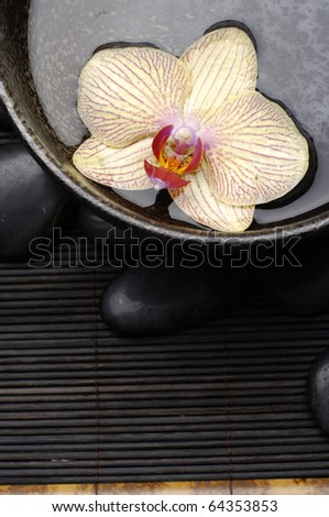 SPA background.- orchid floating in bowl and stones on bamboo stick straw mat