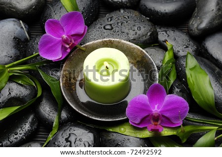 Green candle in bowl with pink orchid and green plant on wet stones