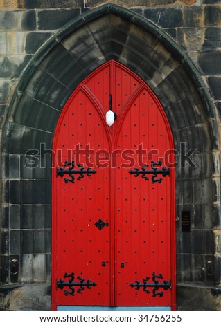 Red church door with black ironwork in a grey stone portal.