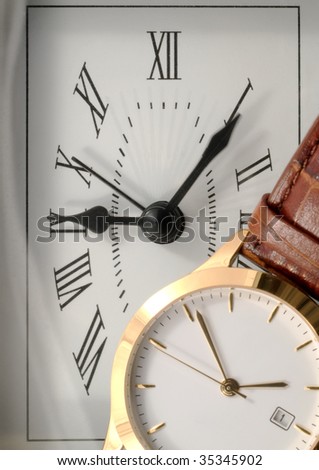 Gold-rimmed wrist watch in front of a clock.