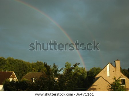 double rainbow in a dark sky over houses and trees in an urban area