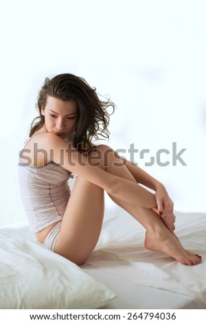 Young adult woman sitting cross-legged on a bed in the morning
