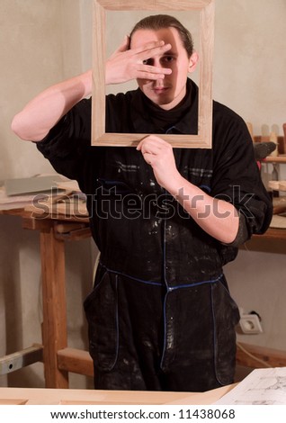 Young carpenter gesturing with hands and holding frame in his workshop