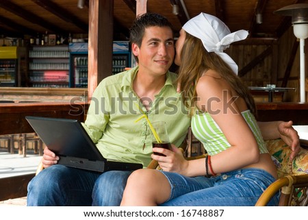 Young woman whisper something to her boy friend in restaurant with laptop