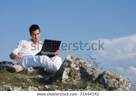 Young man using his laptop sitting on top of the mountain