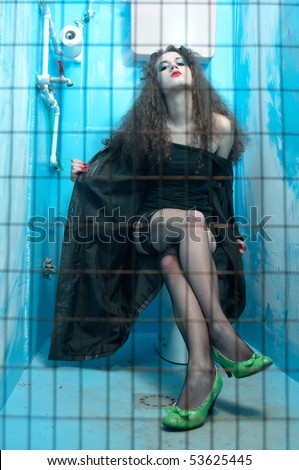Woman sitting on toilet bowl in neglected and dirty public blue toilet behind bars