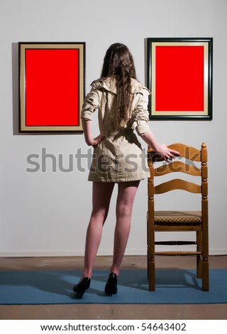 Woman standing inside a gallery infront of two picture frames and looking at them.