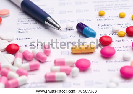 Pen, pills variety and medical certificate form that requires to fill out his required information. Focus on blue capsule