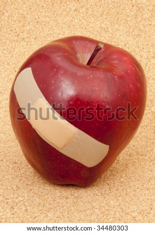 A red apple with a band-aid. Symbolic of problems in the education system or fruit industry. Also would work for a problems with health care theme.  Shot in studio on a cork background.