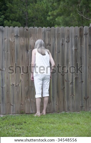 Woman looking through a peephole in a fence to spy on her neighbors!