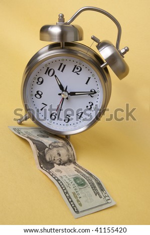 Time is money with this $20 bill (American paper currency) and a silver retro style alarm clock isolated on a yellow background.