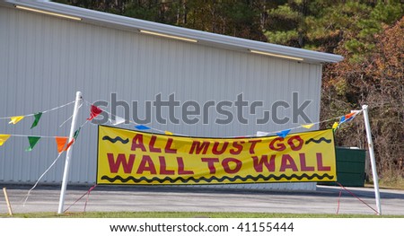 Bright yellow and red all must go wall to wall sign in front of a warehouse.  When the economy is bad, businesses close.