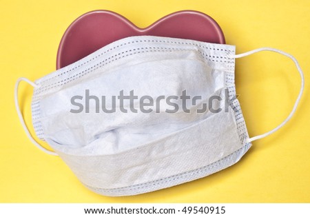 Surgical Mask over a Heart on a Yellow Background.  Good image for heart health or surgery.